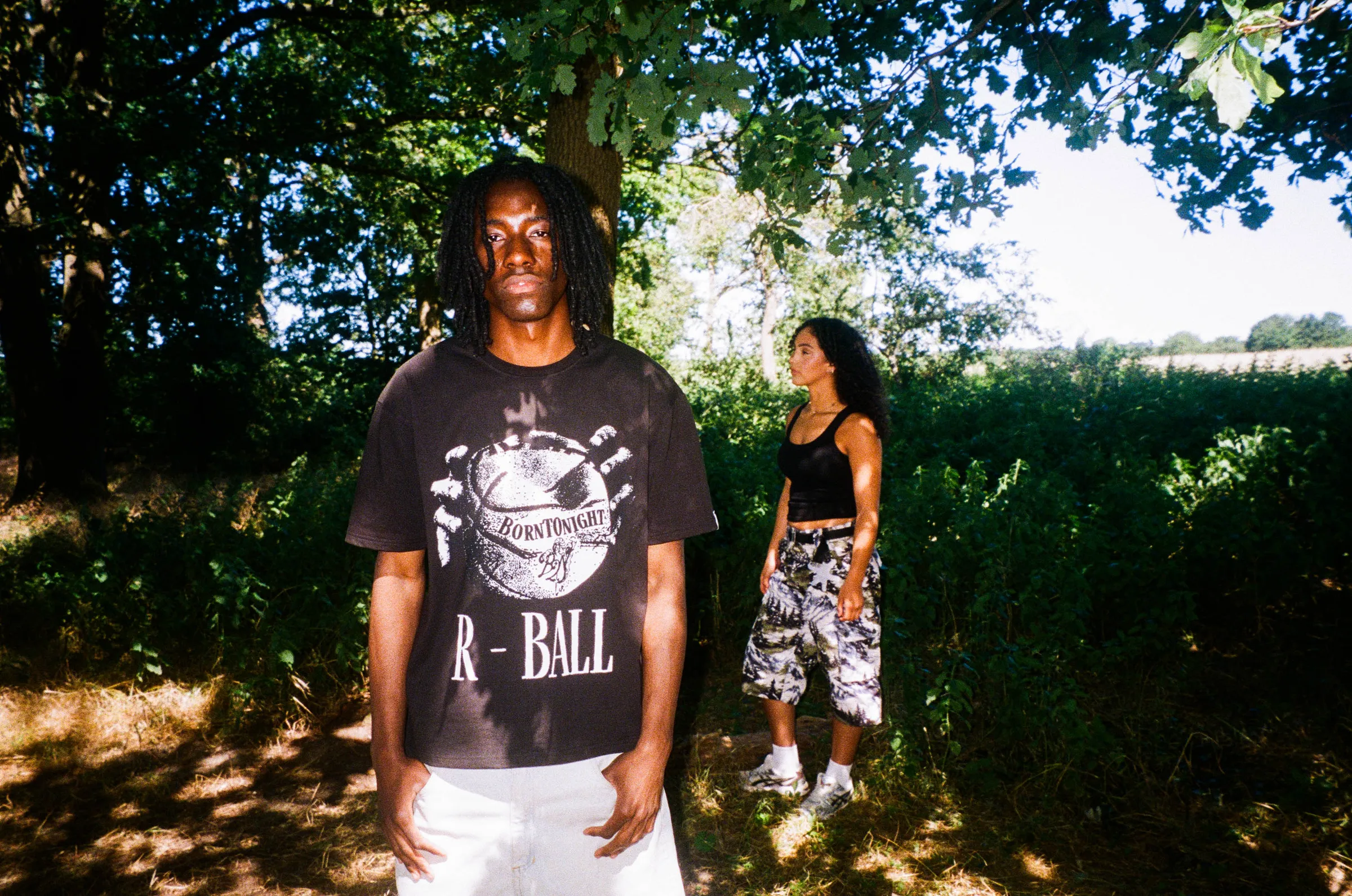 Deux mannequins en sous-bois, t-shirt oversize noir R-BALL et short cargo MOUNTAIN à imprimé montagne
