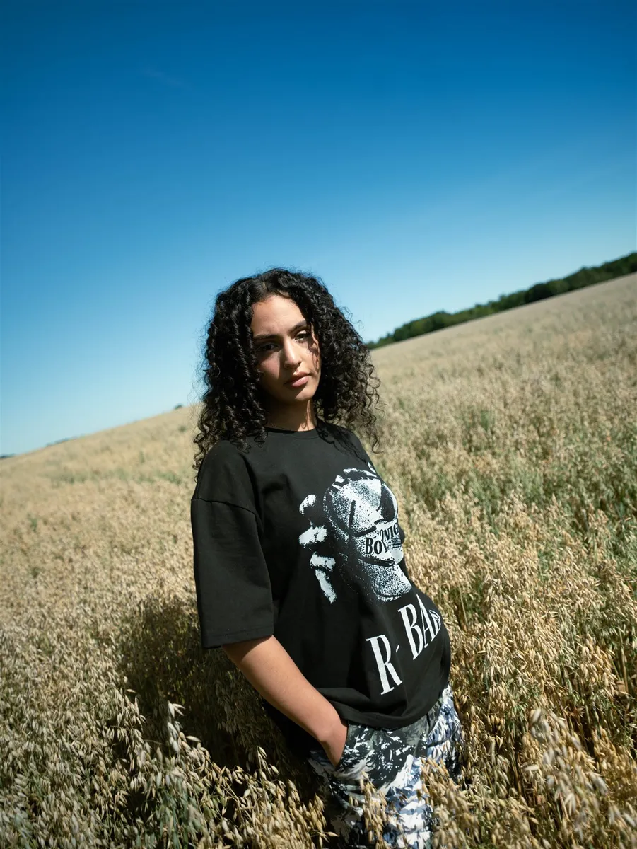 Femme en t-shirt R-BALL debout dans un champ d’avoine, ciel bleu