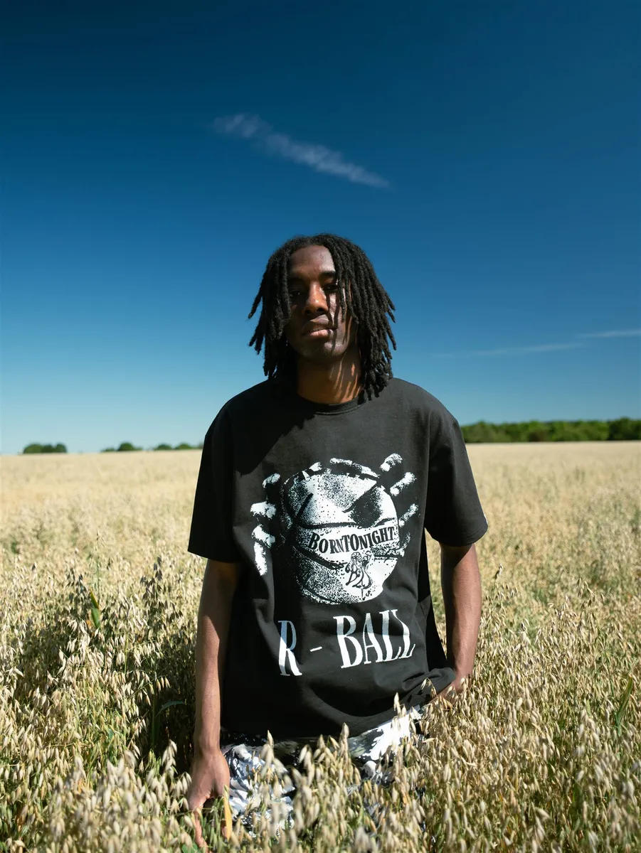 Homme en t-shirt R-BALL debout dans un champ, ciel bleu