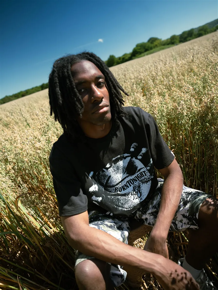 Homme accroupi dans un champ, t-shirt R-BALL