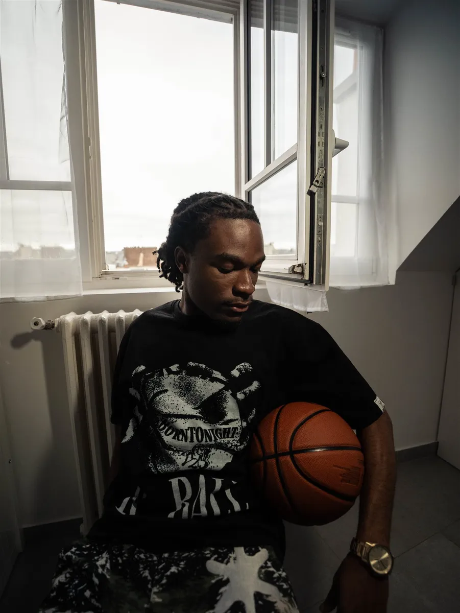 Homme assis près d’une fenêtre, ballon de basket sous le bras