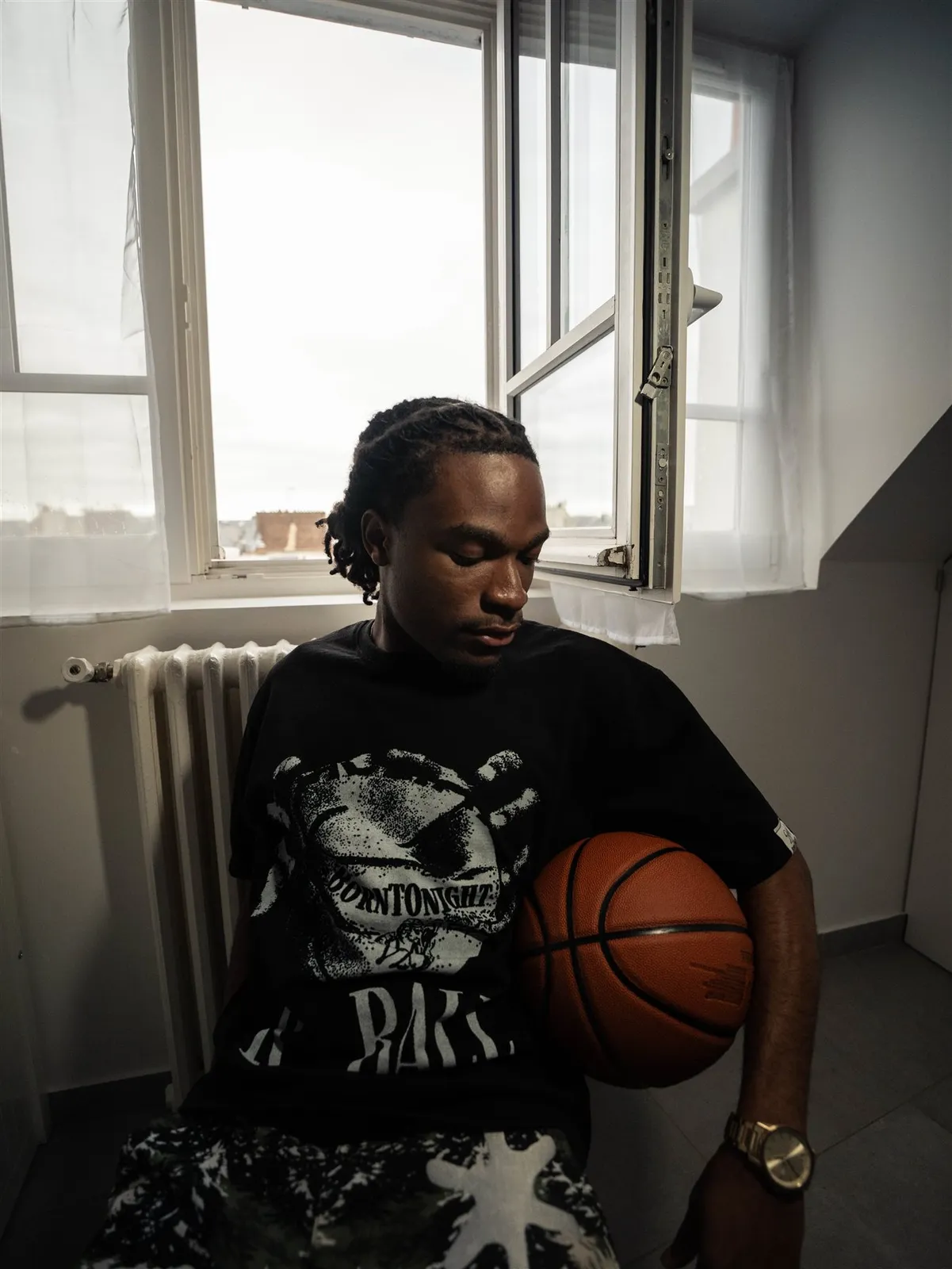Homme assis près d’une fenêtre, ballon de basket sous le bras