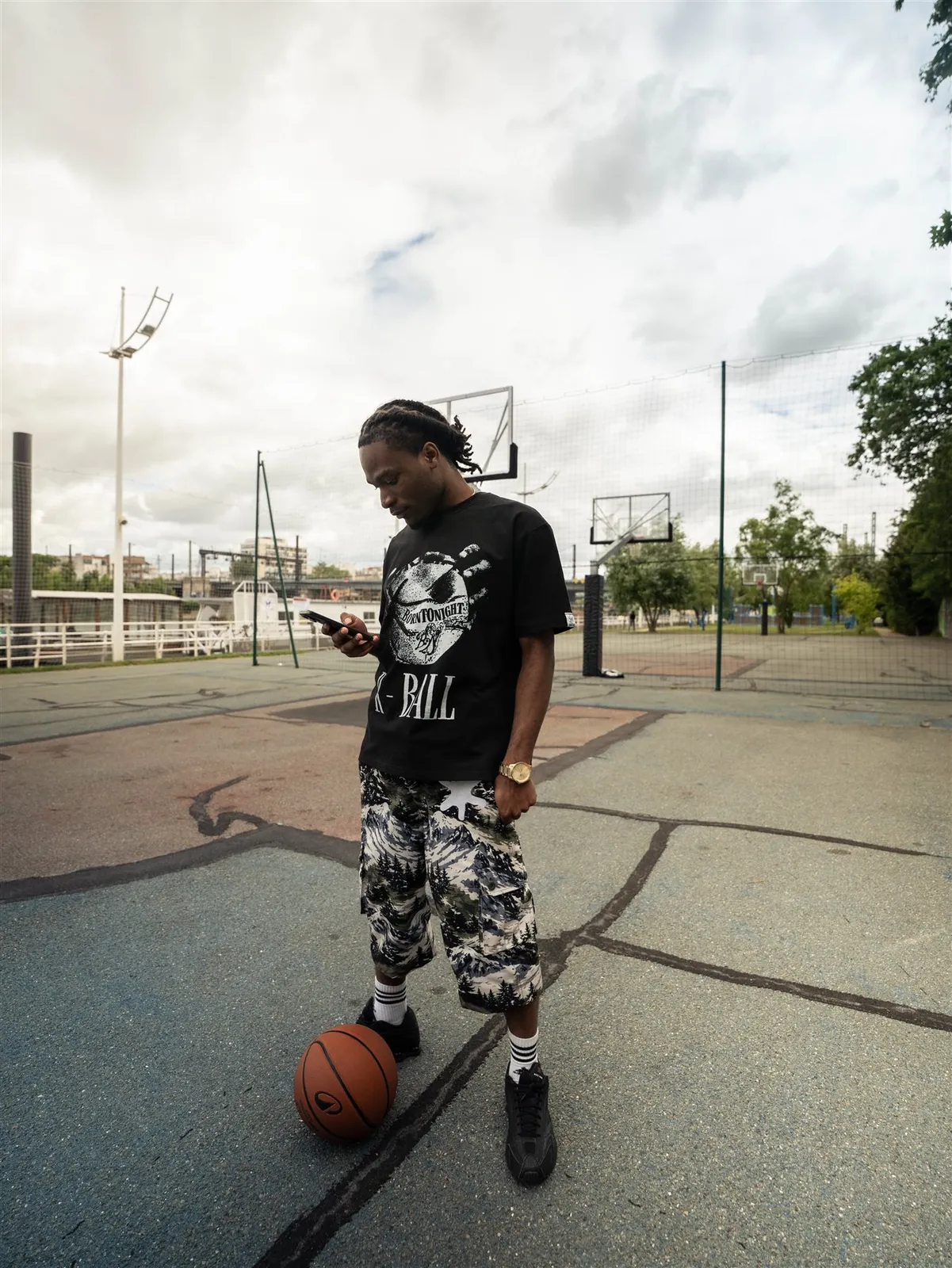 Homme sur un terrain de basket, ballon au pied, téléphone en main