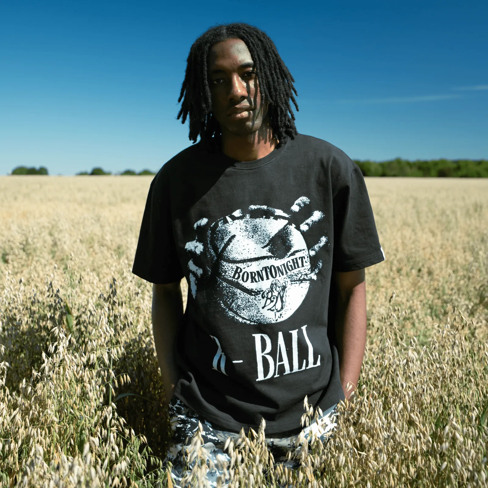 Homme portant le t-shirt oversize noir R-BALL dans un champ d’avoine